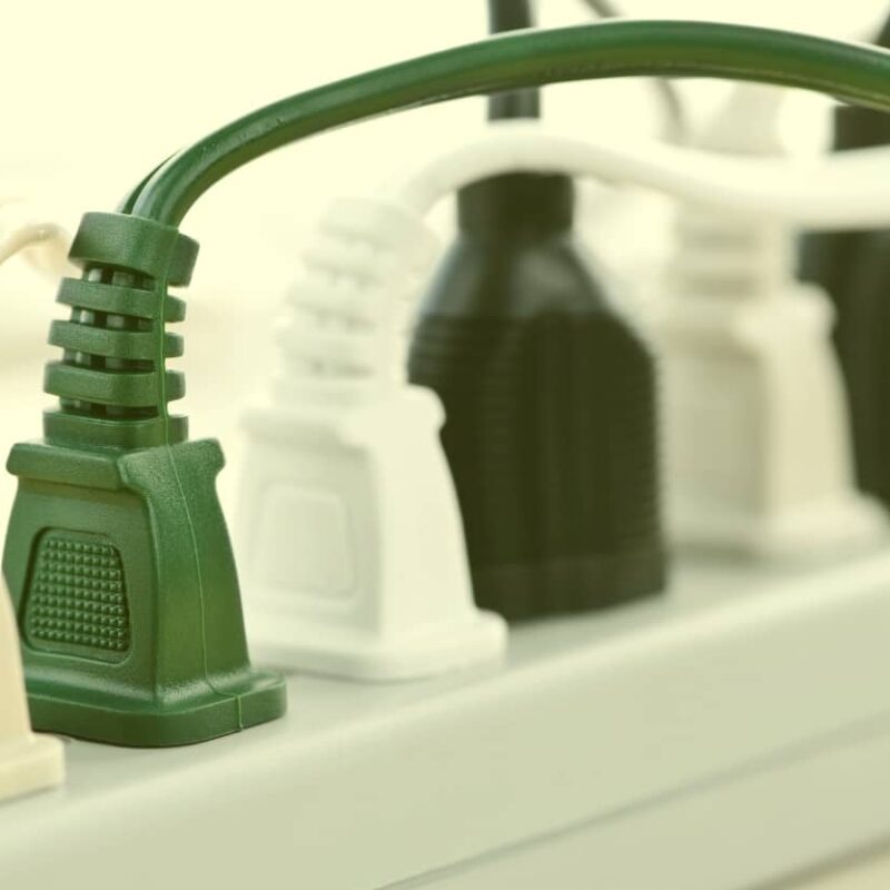 A close-up view of several green, white, and black electrical cords plugged into a white power strip.