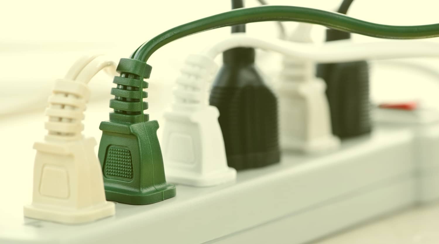 A close-up view of several green, white, and black electrical cords plugged into a white power strip.